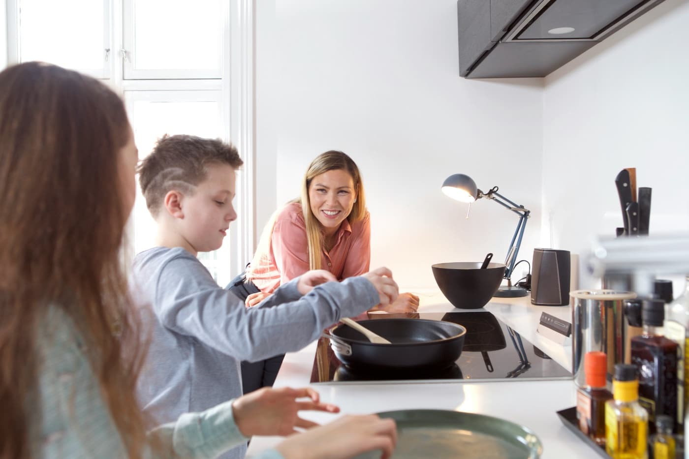 A mother smiling as her children cook together in the kitchen
